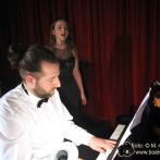 Mann und Frau treten bei einem Musikereignis vor einem roten Bühnenhintergrund.